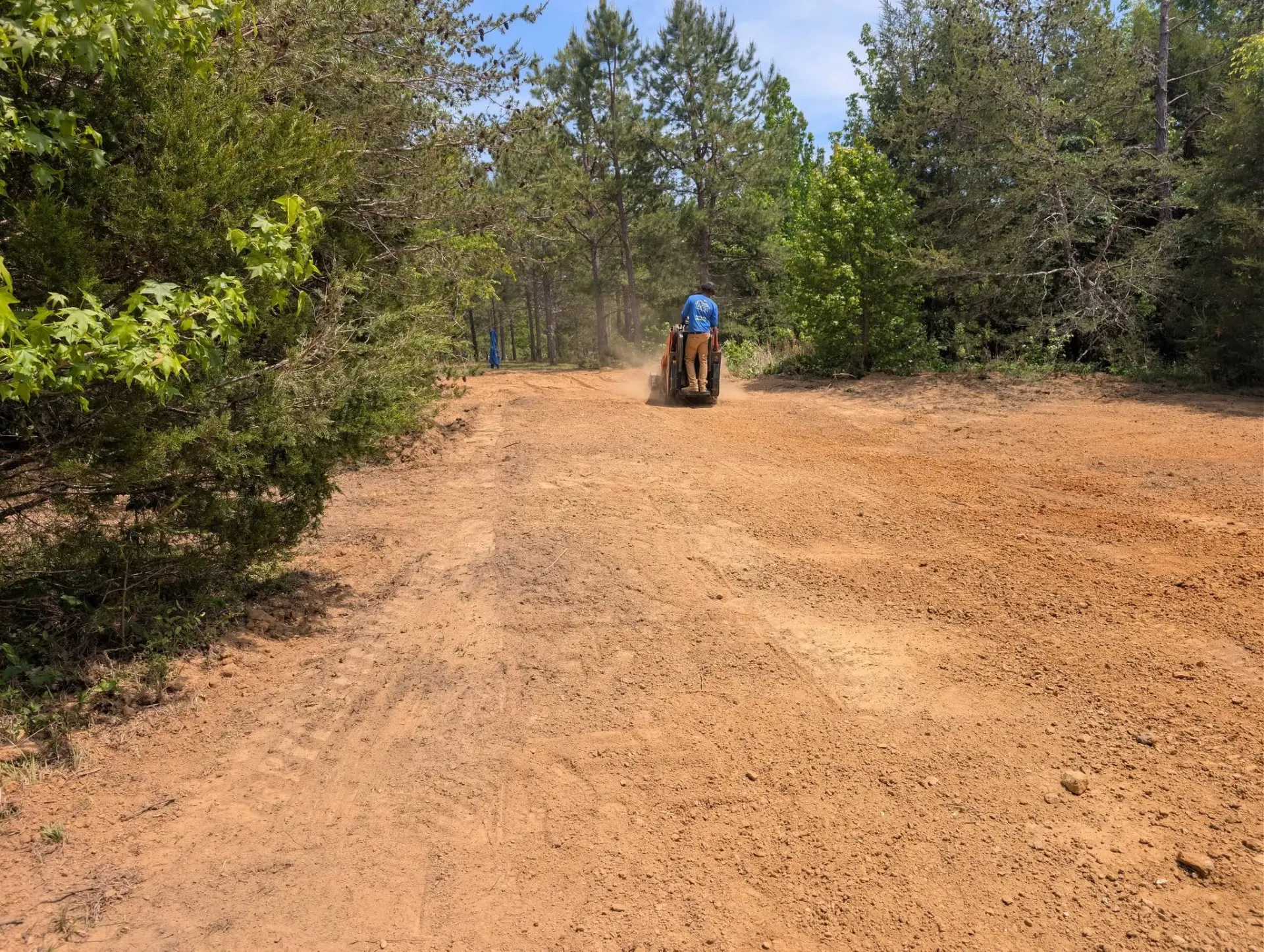 Operator grading a wide dirt access road through the woods
